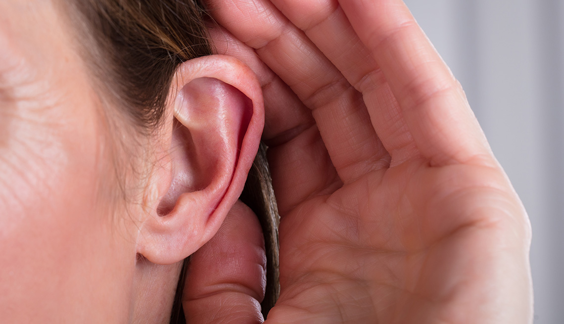 A woman with her hand around her ear listening
