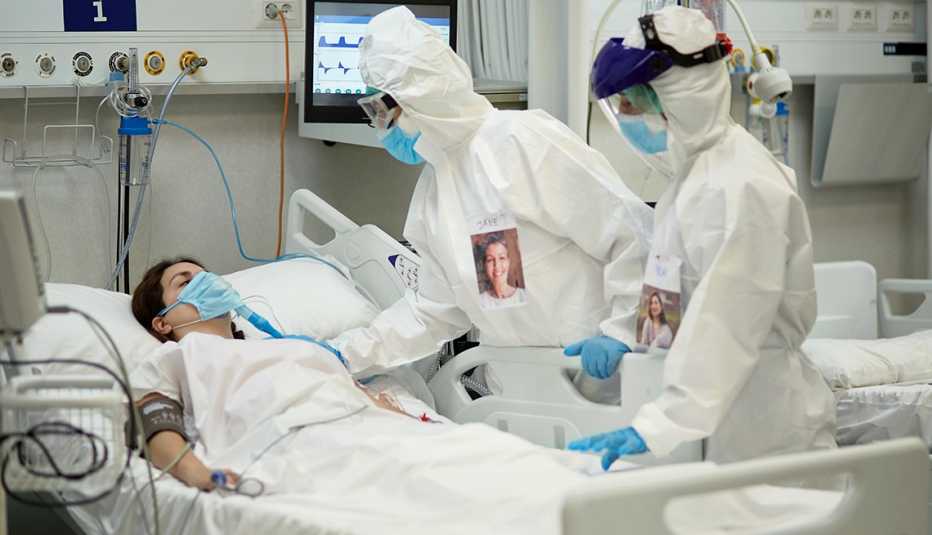 COVID-19 patient lying in a hospital bed with medical staff in protective suits nearby. 
