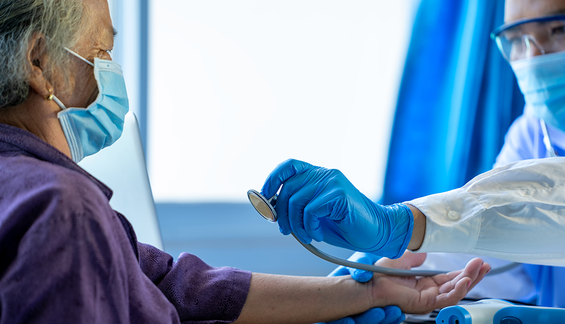 Doctor checking woman's heart and pulse. Both are wearing face masks.