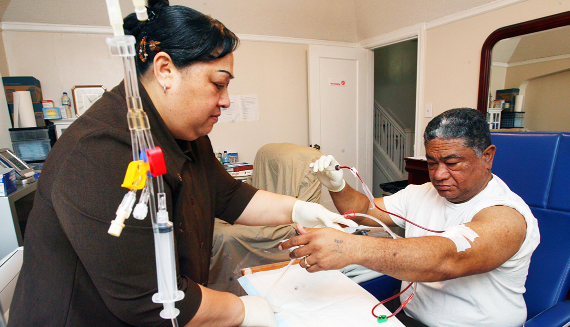 A woman helps hook up a man's dialysis machine in their living room