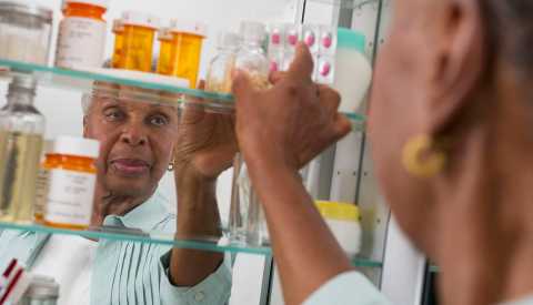 woman removing a bottle of pills from the medicine cabinet woman removing a bottle of pills from the medicine cabinet