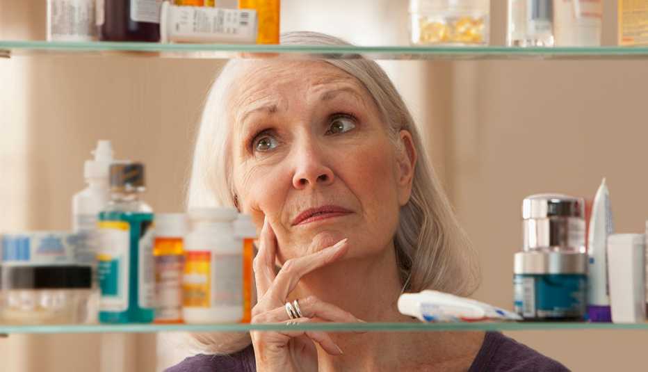 Woman looking thoughtfully into her medicine cabinet Woman looking thoughtfully into her medicine cabinet