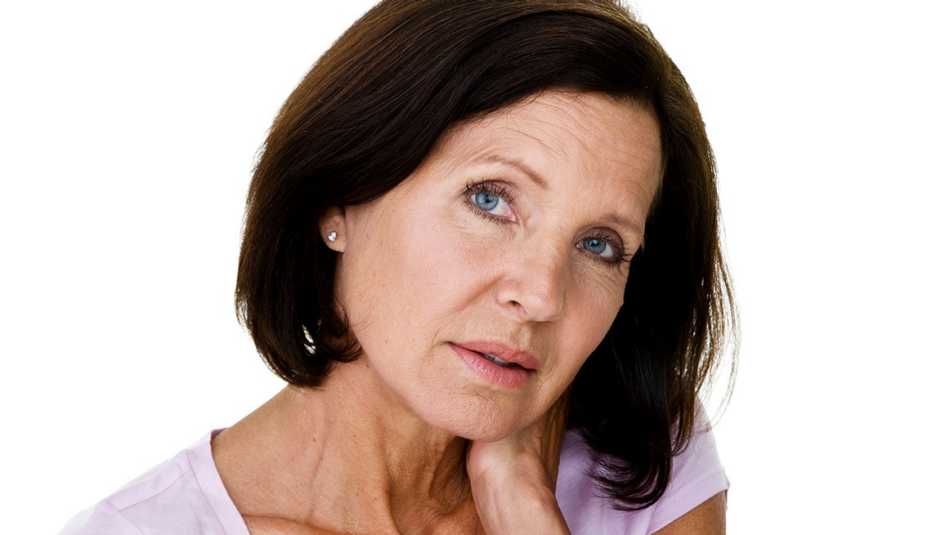 Mature woman in pink shirt touching her neck looking concerned or uncomfortable.