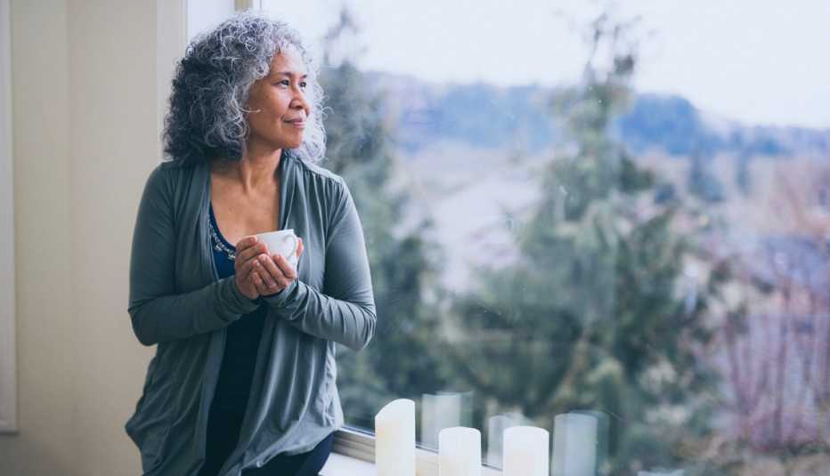 a woman looking out a window and drinking coffee