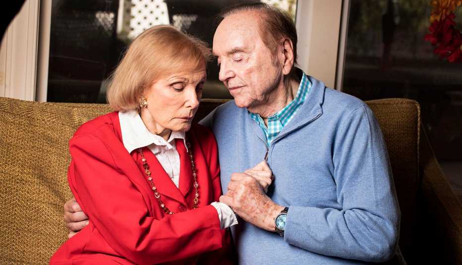 Warren Adler sits with his wife on the couch, holding hands
