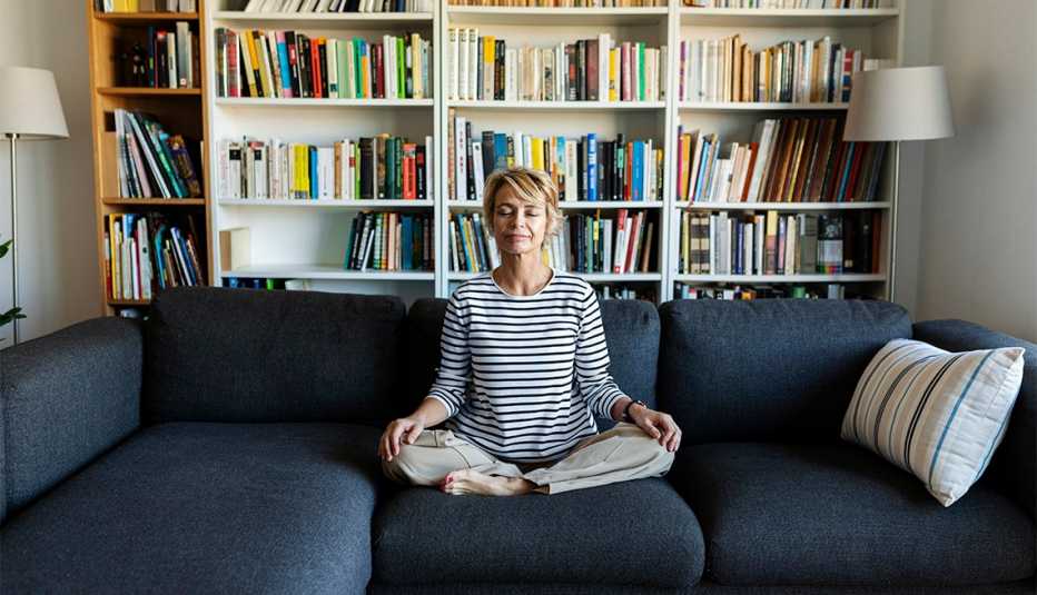 Mature woman practicing yoga on couch at home