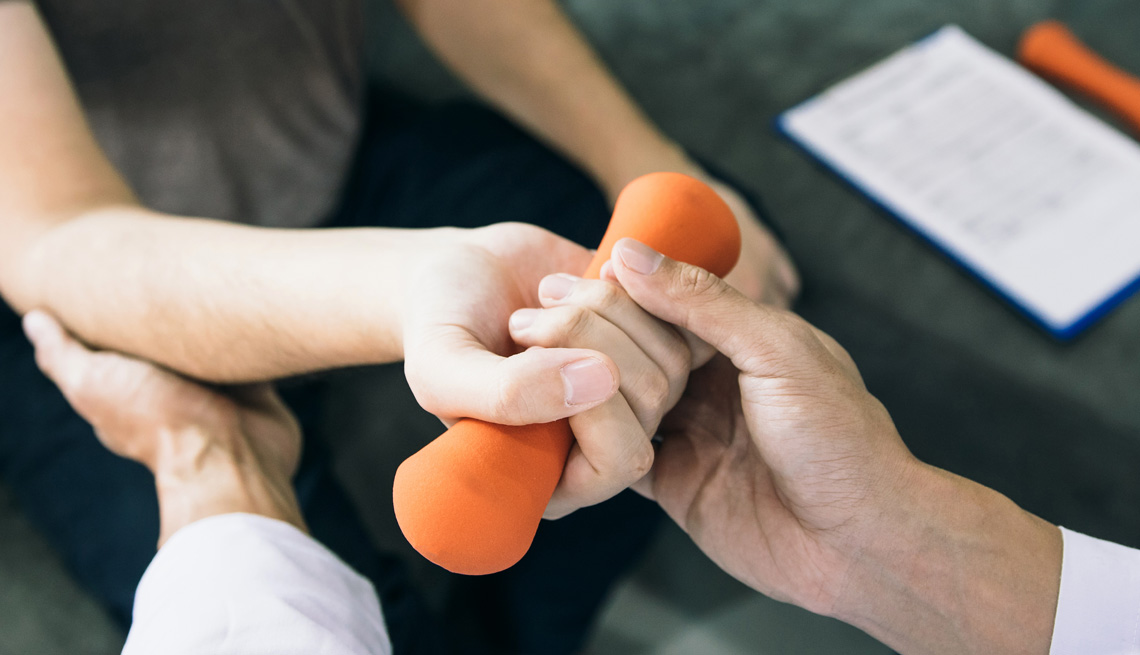 a woman holding a dumbbell while someone helps position her arm
