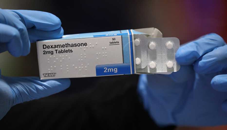 A pharmacist wearing protective latex gloves handles a packet of dexamethasone