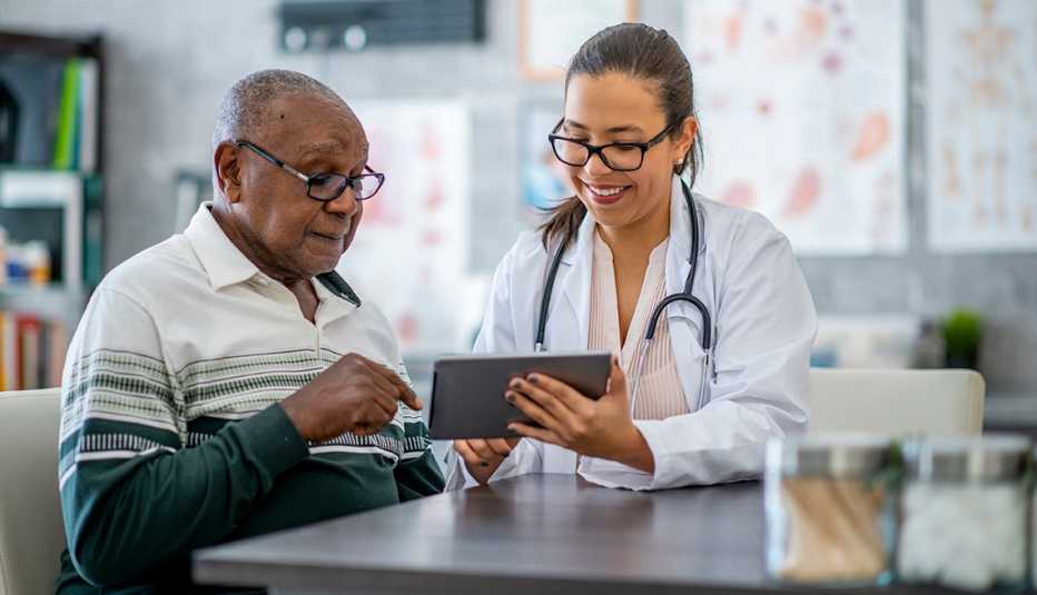 A man is sitting in his doctor's office and listening as the doctor shows him something on a digital tablet