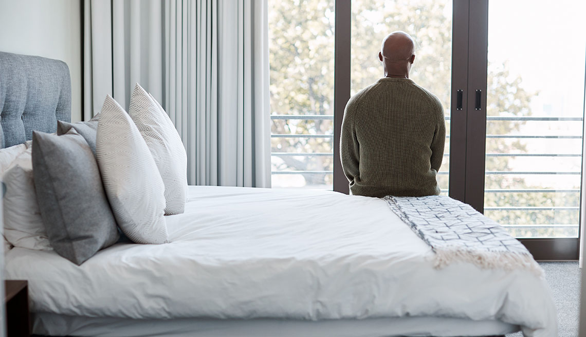 rear shot of a man looking through a window in a bedroom