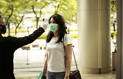 security guard measuring temperature of young woman  with infrared thermometer before entering a office
