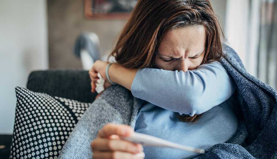woman sneezing and checking her temperature