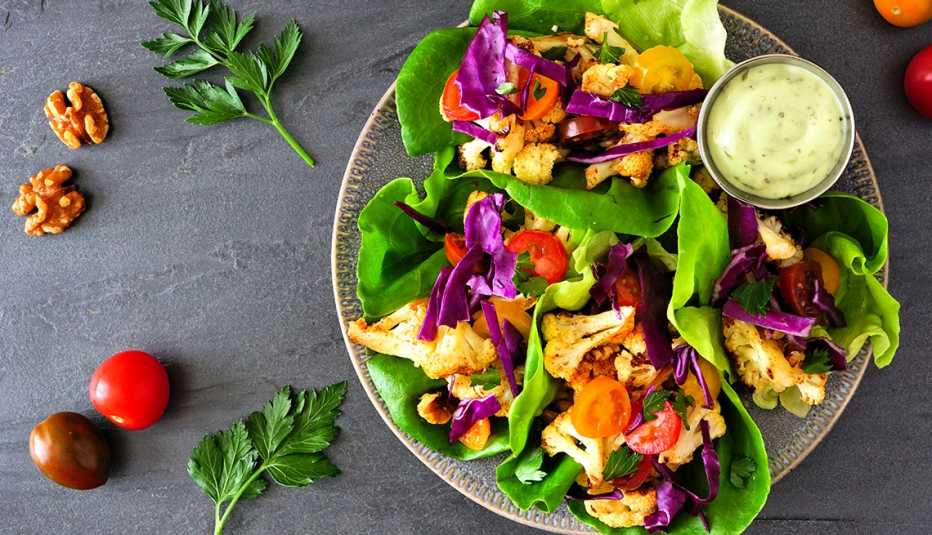 Healthy lettuce wraps with grilled cauliflower, cabbage and tomatoes. Top view over a dark slate background. Plant-based diet concept.