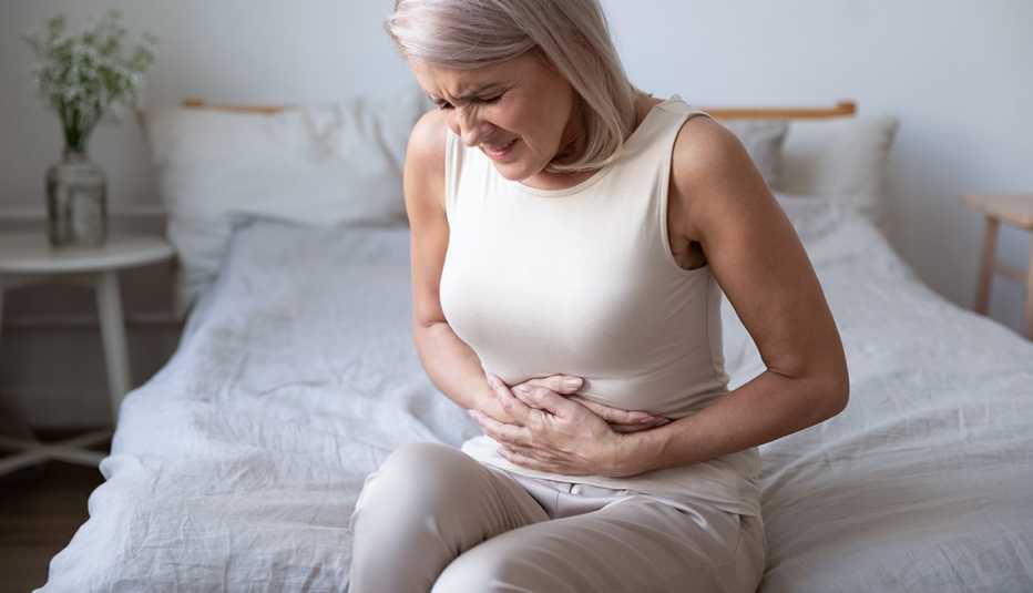 a woman sits on the edge of her bed holding her abdomen as if in pain