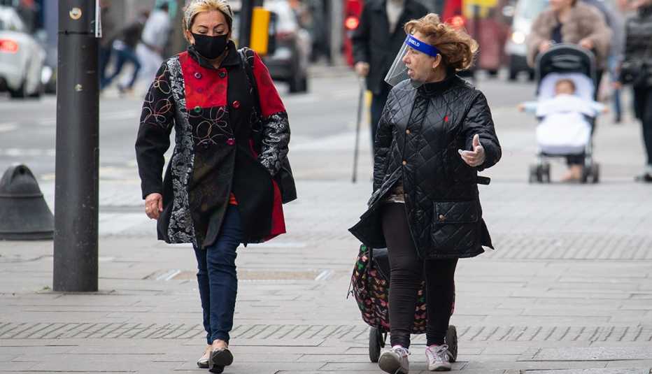 Two women wearing a protective face mask and a plastic face shield on a London street. Two women wearing a protective face mask and a plastic face shield on a London street.