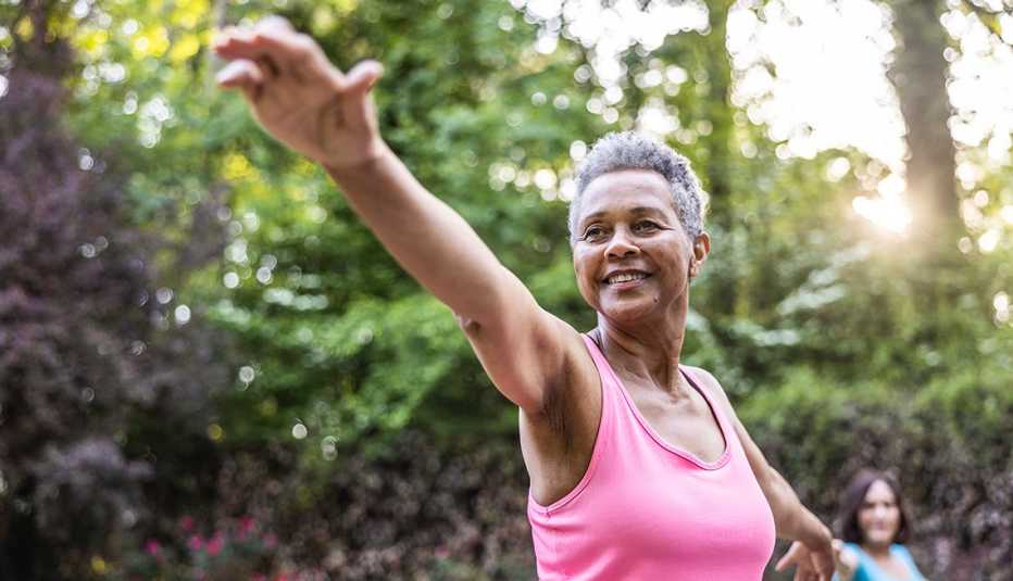 a woman in a pink shirt enters warrior pose in an outdoor yoga class with a friend