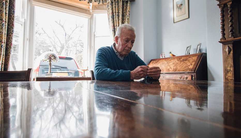Senior man is sitting alone at the dining table in his home, with a worried expression on his face.