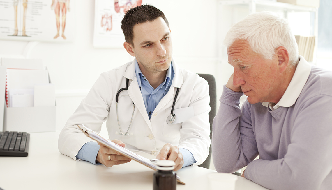 A man appears unhappy with his hand to his face during a visit with his doctor