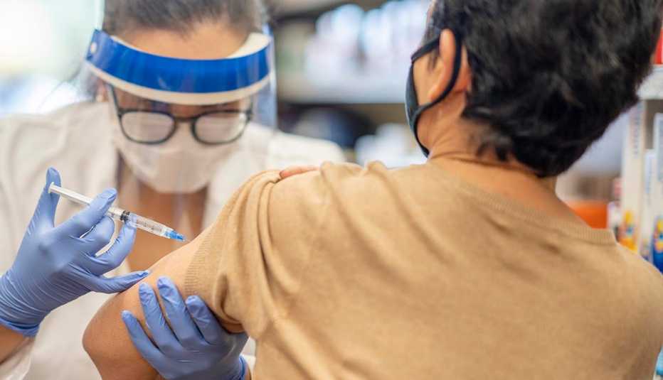 Masked senior woman getting a vaccine while at the pharmacy by a masked female pharmacist.