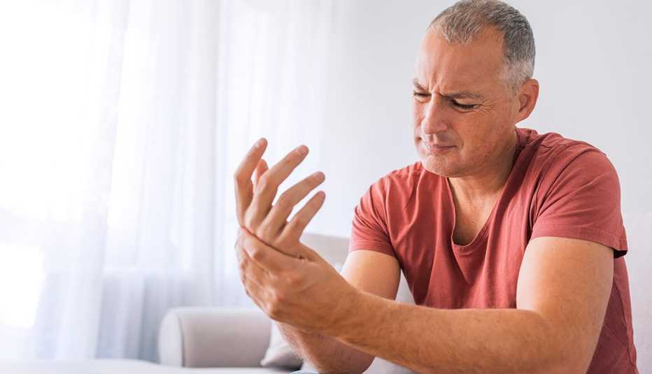 Mature man suffering from wrist pain at home while sitting on sofa during the day. Clenched painful hands Mature man suffering from wrist pain at home while sitting on sofa during the day. Clenched painful hands