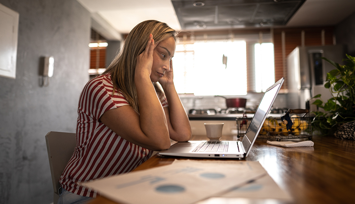 A woman working from home at her kitchen table looking stressed