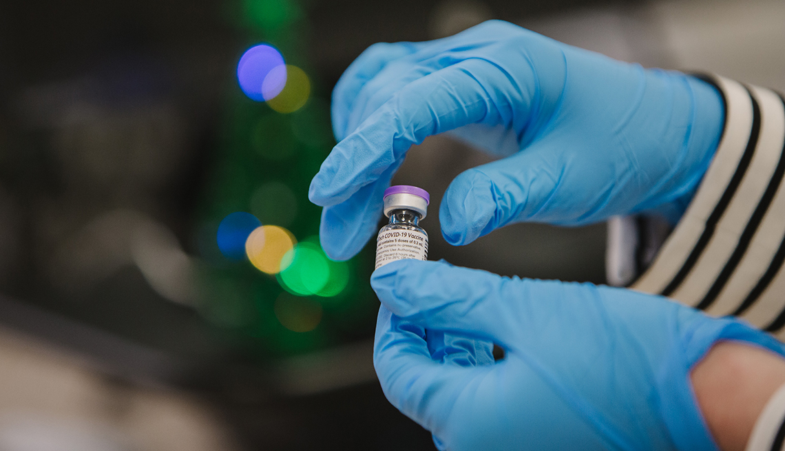 Close up of hands wearing medical gloves holding a coronavirus vaccine vial.