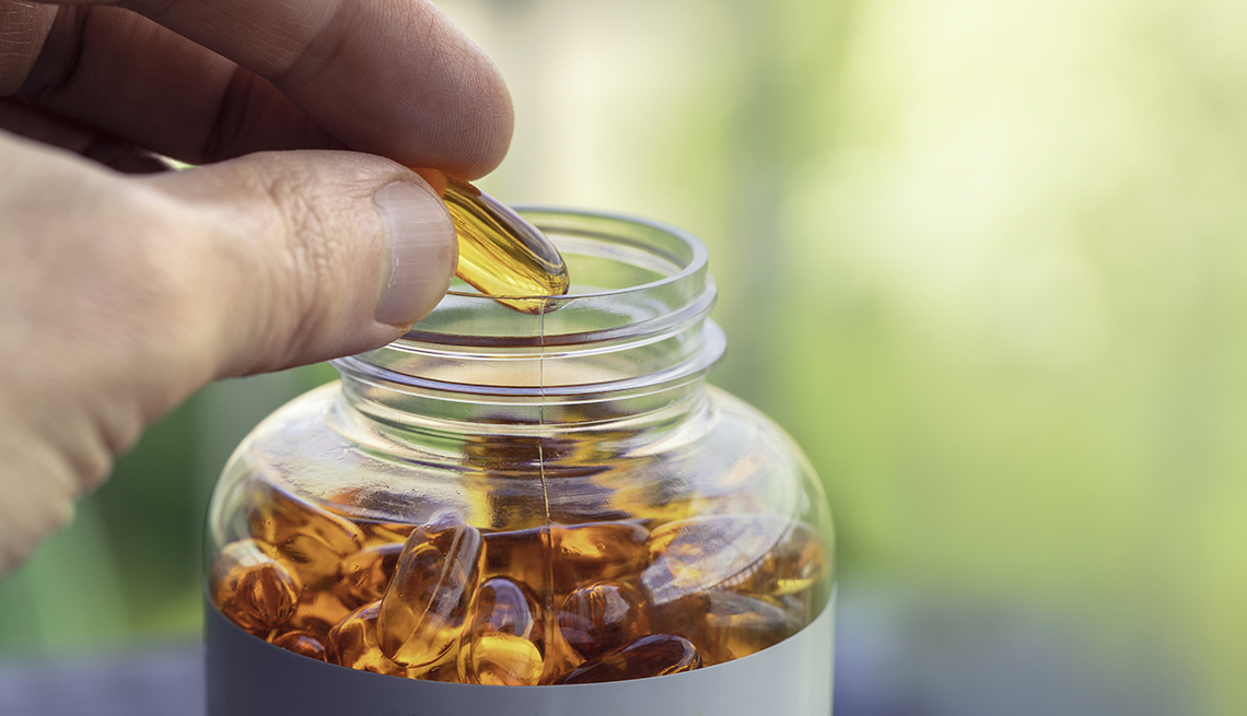 A person taking a fish oil capsule from a pill bottle