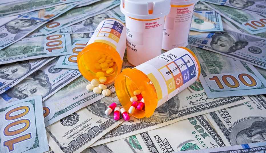 A group of pill bottles and pills on top of a pile of one hundred dollar bills