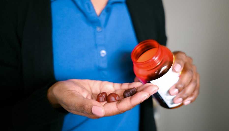 close up of a woman pouring melatonin gummies out of an orange bottle into her hand close up of a woman pouring melatonin gummies out of an orange bottle into her hand