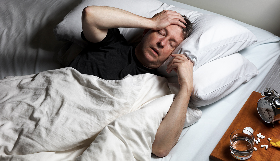 Man in bed experiencing pain with pills on table