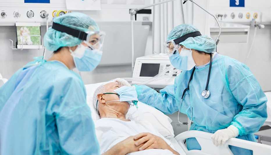 Doctors in protective equipment treat a patient in a hospital bed wearing a mask.