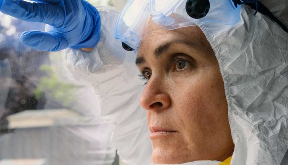 health care worker wearing protective gear looking out a window. She appears sad and stressed.