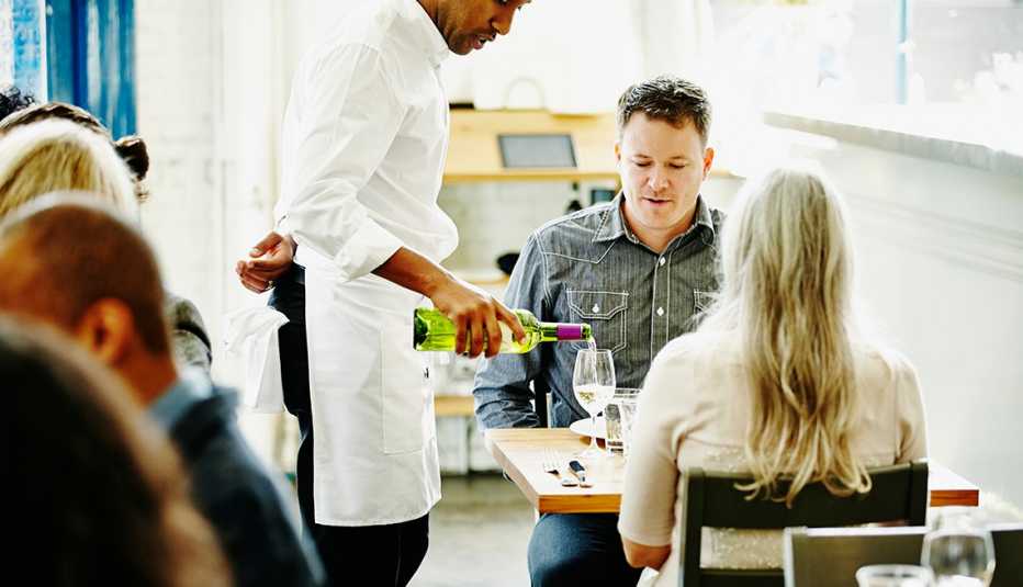 waiter pouring glass of wine for couple dining together in restaurant
