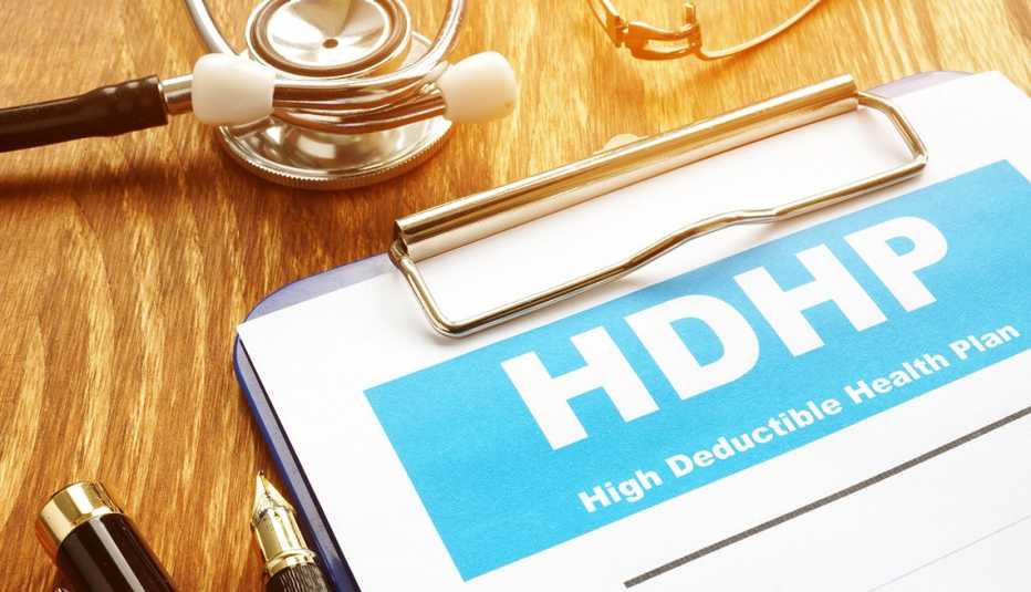 HDHP, High Deductible Health Plan written on paper clipped to board on desktop with stethoscope and pen