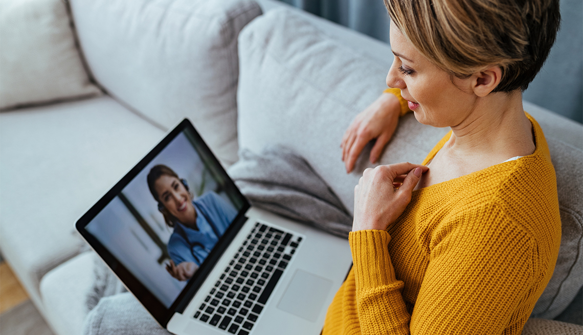 woman sitting on the sofa while talking with her doctor over a laptop.