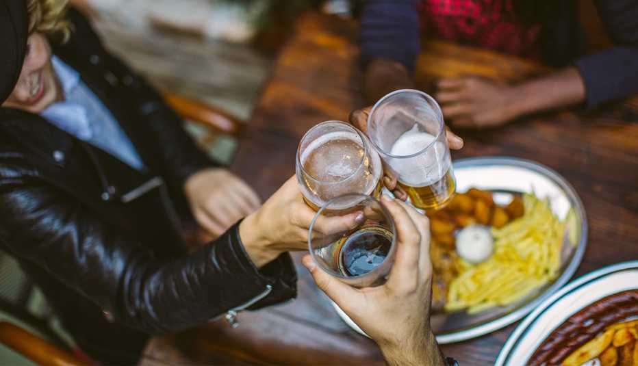 view from above three people toasting each other with glasses of beer over plates of food