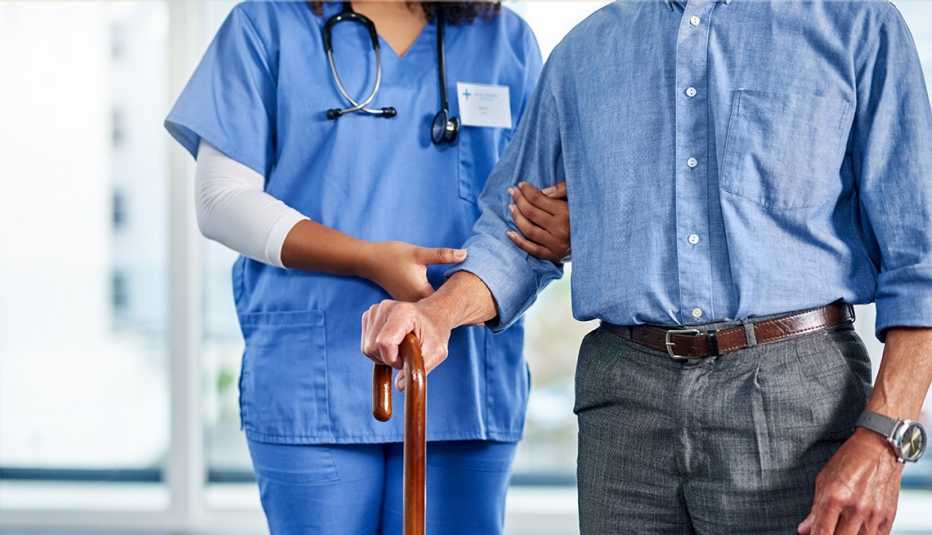 a nurse or physical therapy assistant is helping support an older man walk with a cane