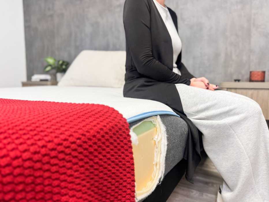 Woman sits on the edge of a mattress with a red blanket
