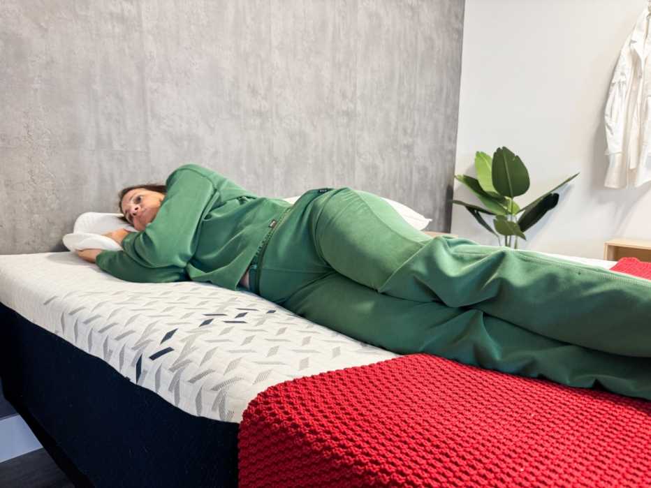 A woman lies on the edge of the mattress with a red blanket