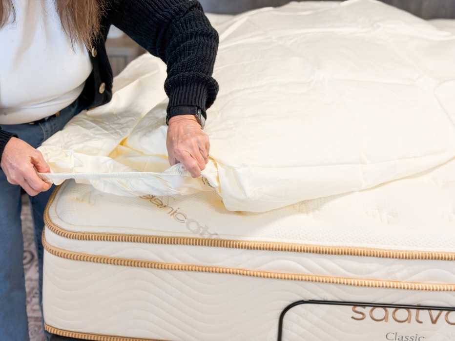 A woman putting the fitted sheet of the Saatva Organic Sateen Sheet Set onto a mattress.