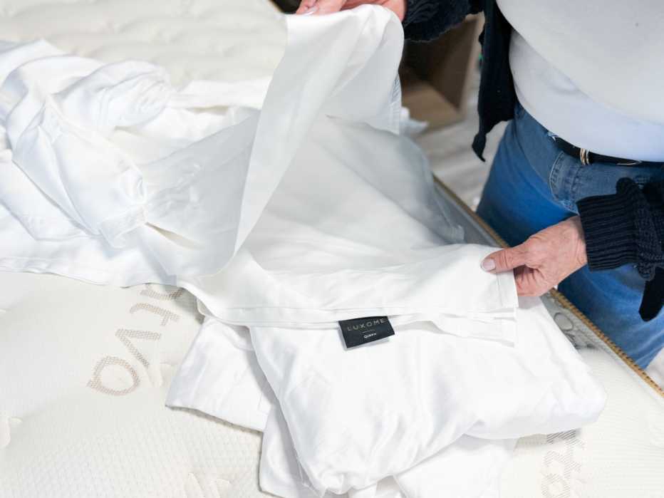 A woman unfolding the flat sheet of the Luxome Luxury Sheet Set