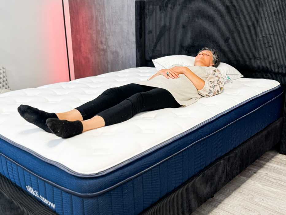 Woman lies on her back in bed with her arms folded on her stomach and eyes closed.