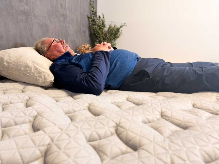 Man lies on his back with his hands clasped on his chest and his eyes closed.
