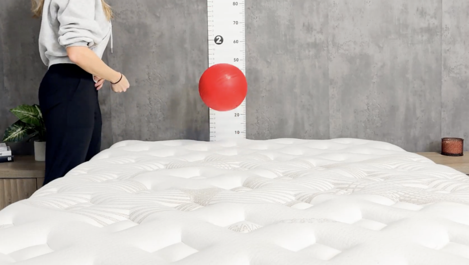 Woman drops a red ball onto a mattress with a ruler behind it to measure how high it rebounds