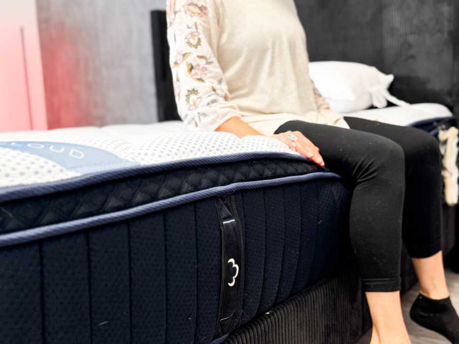 A woman sitting on the edge of the DreamCloud Premier Hybrid mattress to test edge support.

