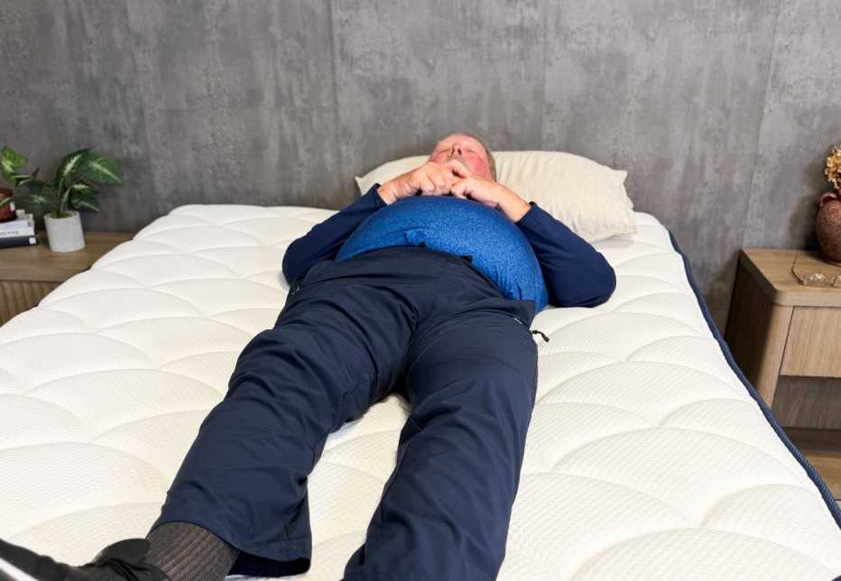 Man lies on his back on a bed with his eyes closed
