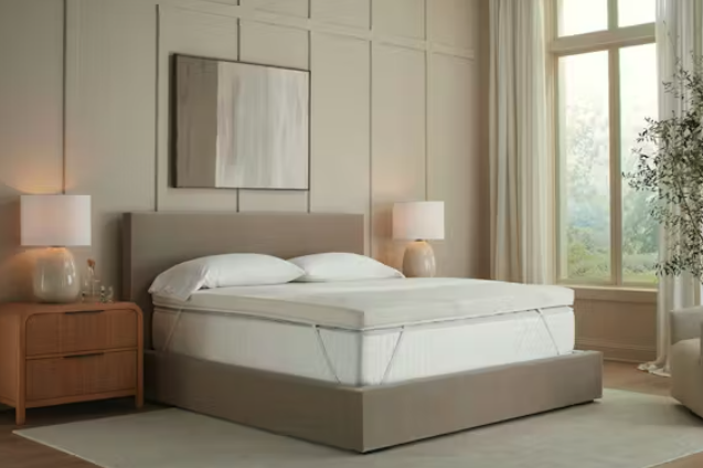 The Saatva Graphite Memory Foam Mattress Topper on a bed in a bright bedroom