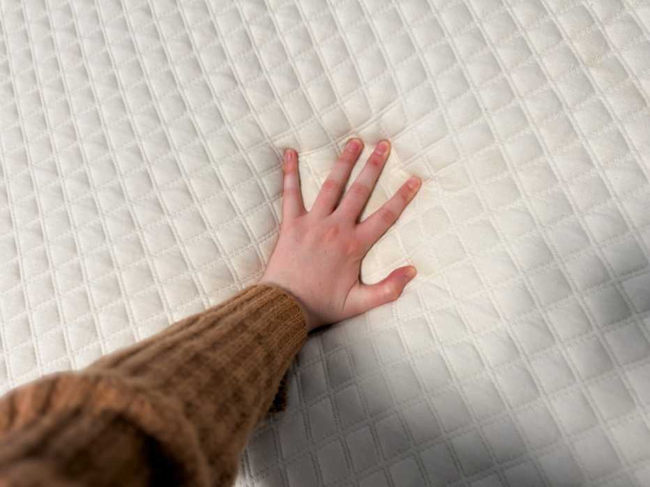 A person pushes their hand into the surface of a quilted white mattress topper