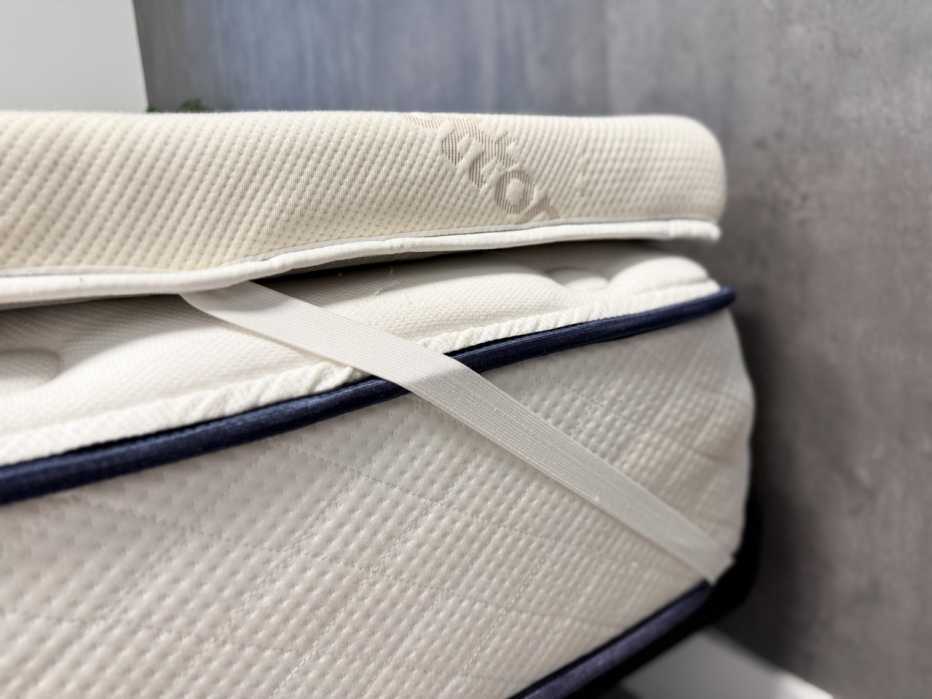 The corner of a mattress with a mattress topper secured by a strap