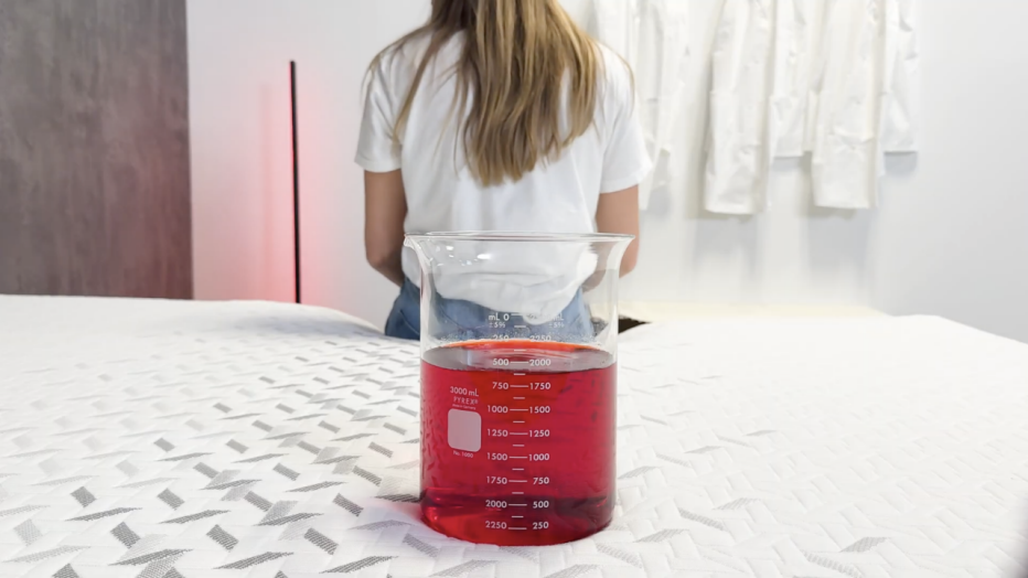 a person sitting on a mattress with a container of red liquid